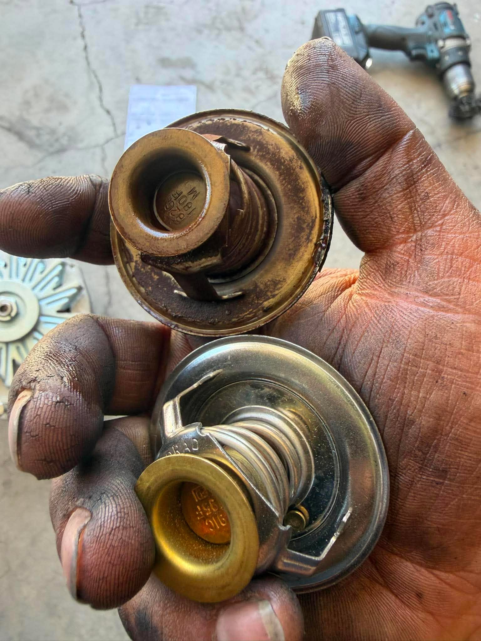 Two thermostats held in hand, showing an old rusted unit versus a new one